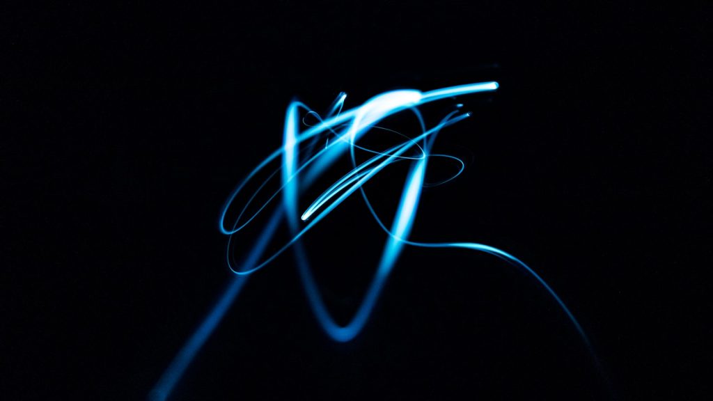 A long-exposure photograph of blue light drawing looping trails against black.