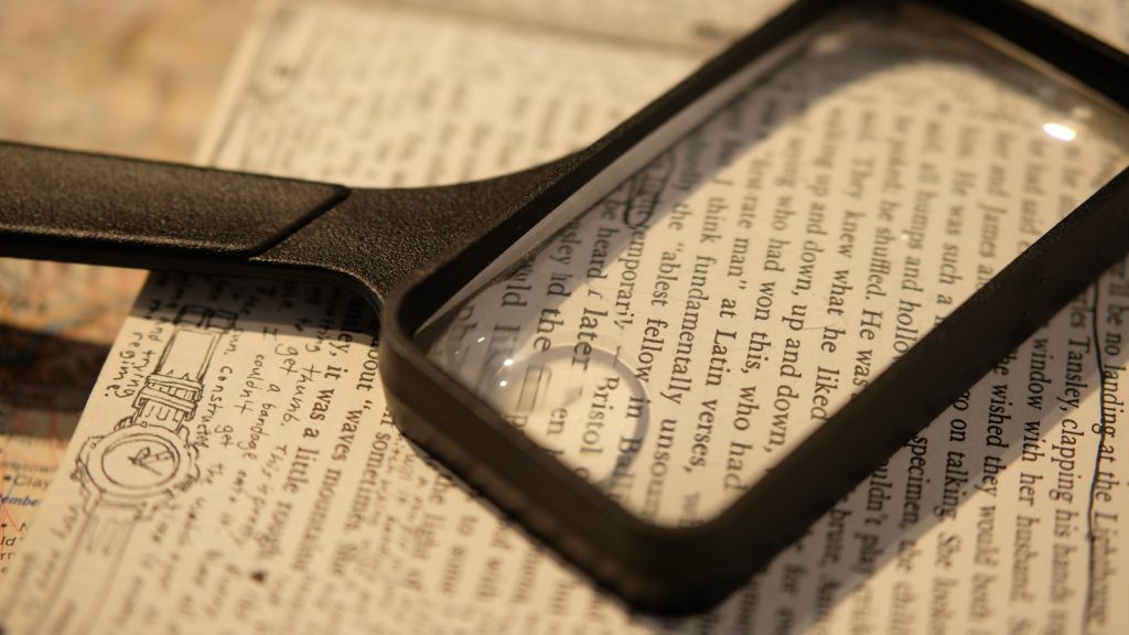 A rectangular magnifying glass resting on the open page of a book, enlarging a few lines of text.