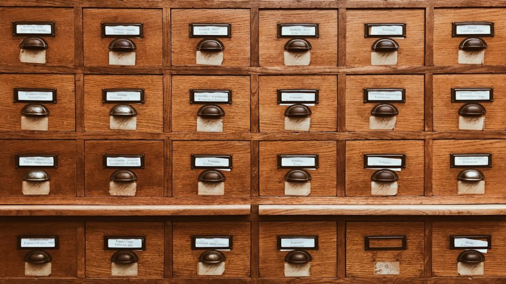 A wall of wooden library card-catalogue drawers, each with a handwritten index label.