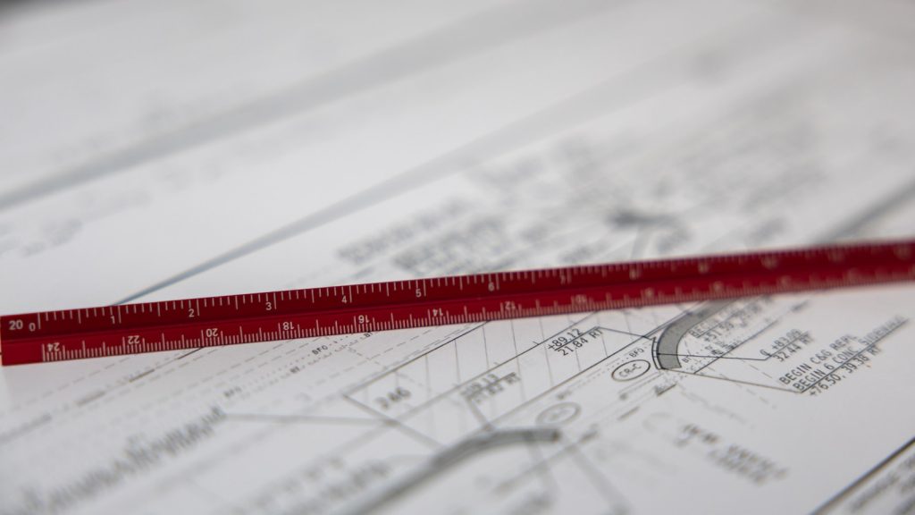 A red scale ruler lying across a set of printed engineering drawings.