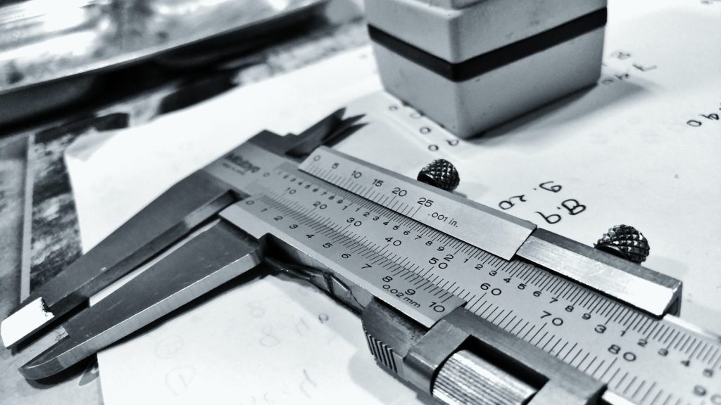 A vernier caliper resting on a workshop drawing, its measuring scale in sharp focus.