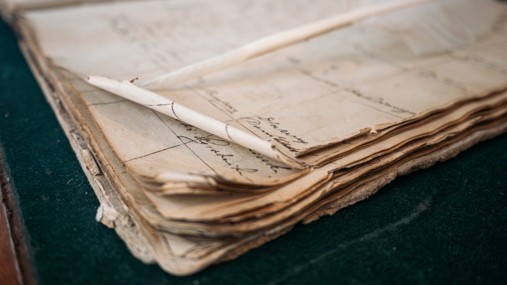 A weathered ledger lying open at a page of handwritten entries, a quill resting across it.