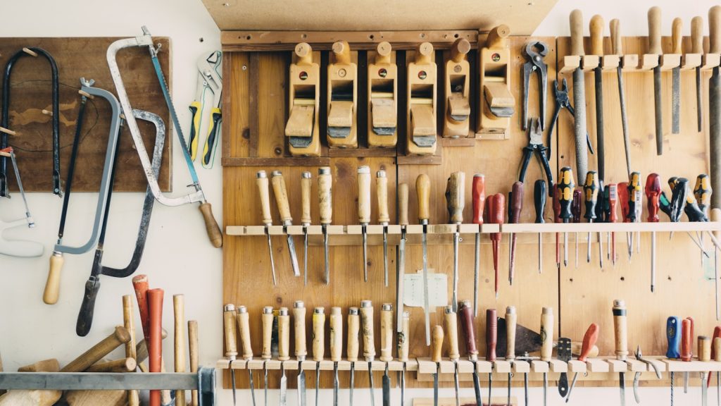 A workshop wall hung with chisels, saws, hand planes and screwdrivers arranged in neat rows.